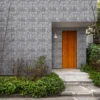 Fachada de vivienda amplia, puerta de madera, arbustos al rededor y enchapado de cerámica piedra Pedral, colección Ecos de Cerámicos Gala